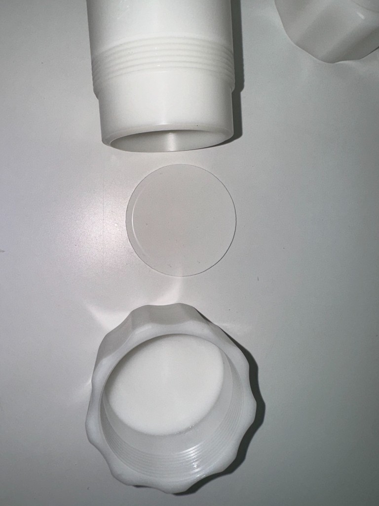 Machined white plastic vial with external threads, a circular sealing disc, and a scalloped threaded cap