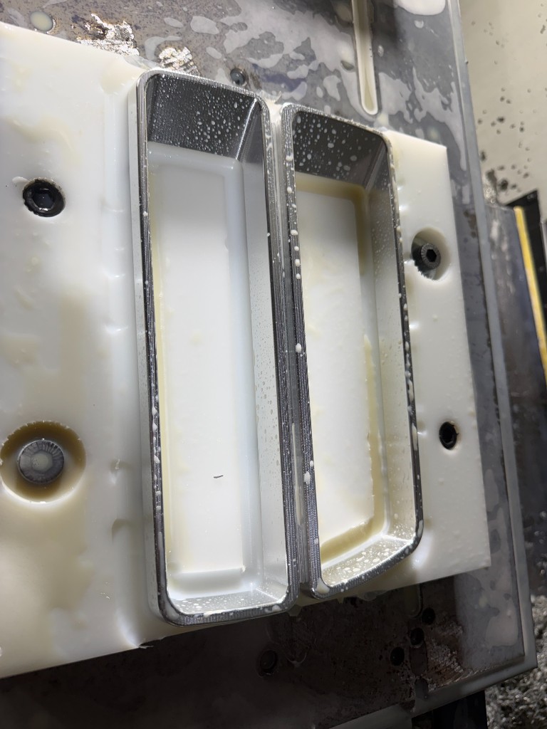Two reverse-engineered classic-car taillight bezels still clamped in a white plastic fixture on the mill