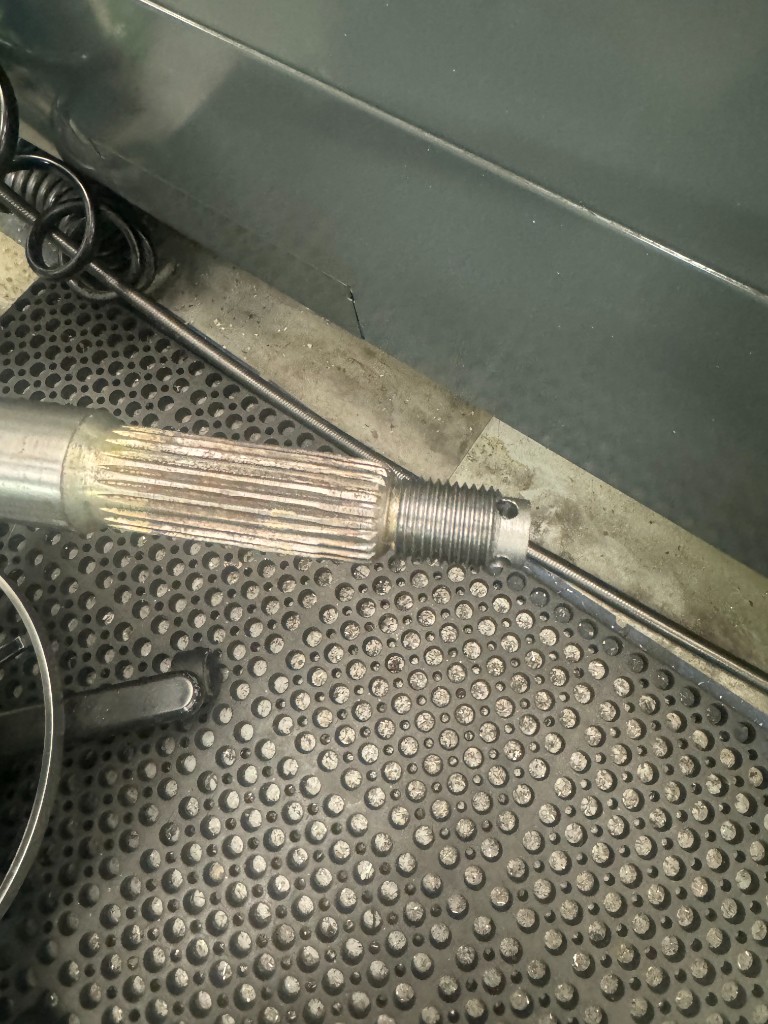 Worn splined shaft with a threaded end and a cross-drilled pin hole, photographed on the shop floor